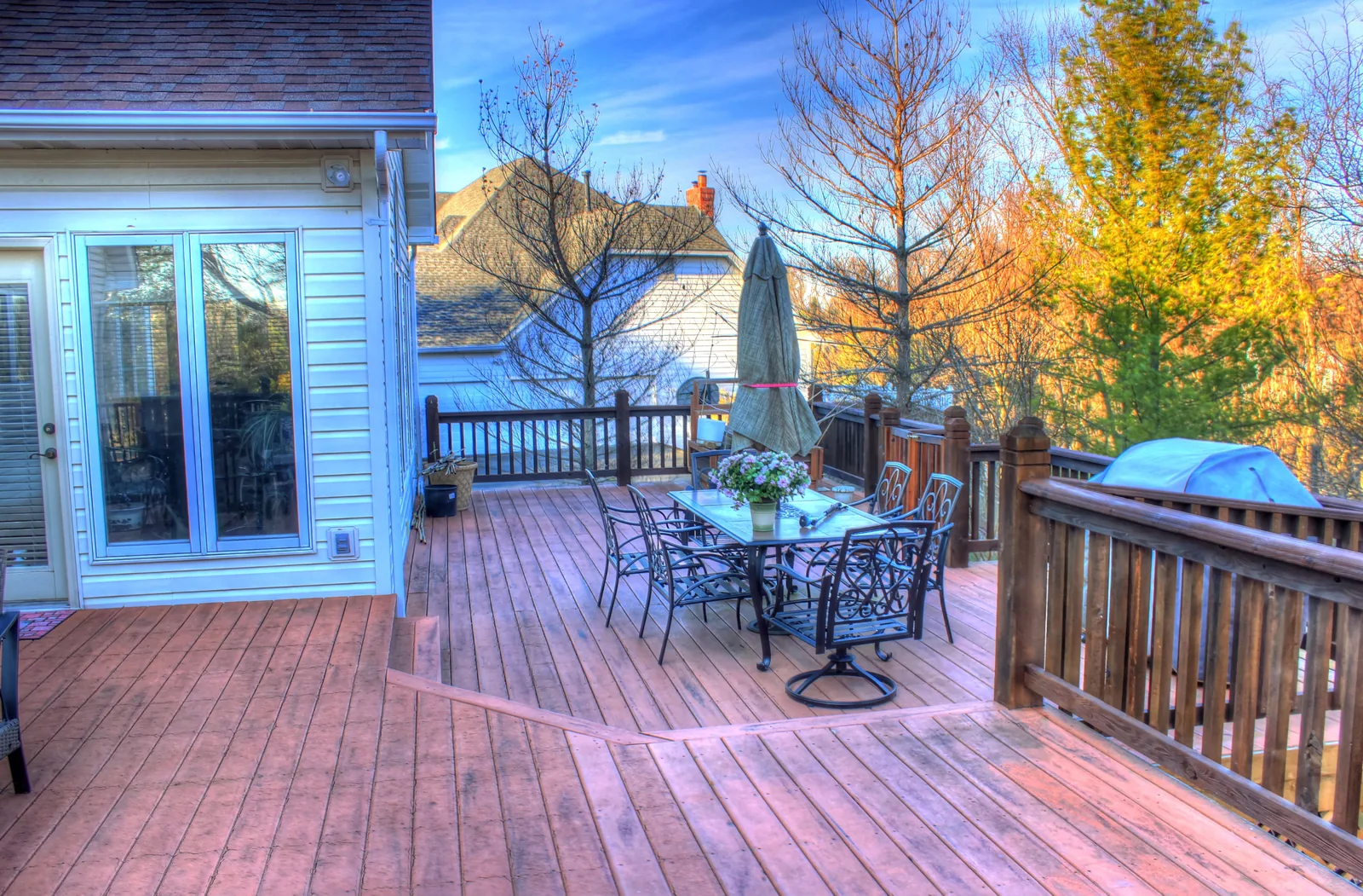 Multi-level backyard wood deck with stained railings, a patio dining set and umbrella beside the house