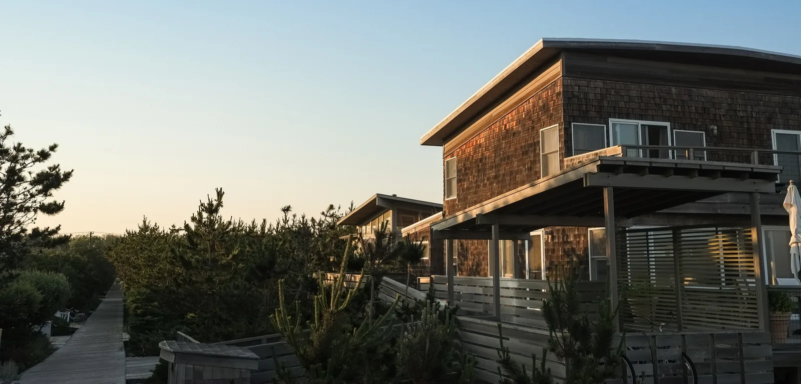 Cedar-shingled house with an elevated wood deck, balcony railing and slat privacy fence in evening light