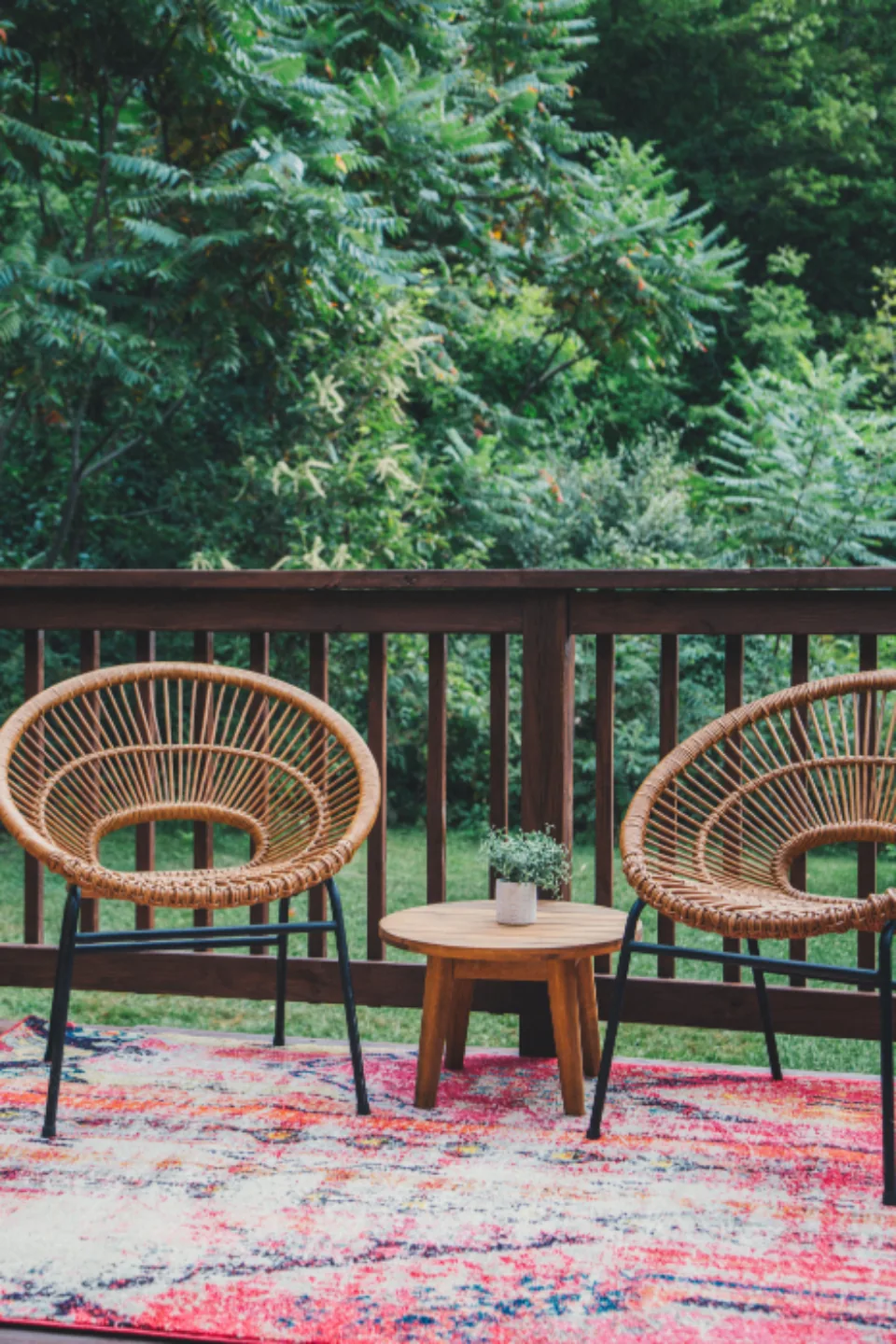 Two rattan chairs and a side table on a deck with a dark-stained wood railing