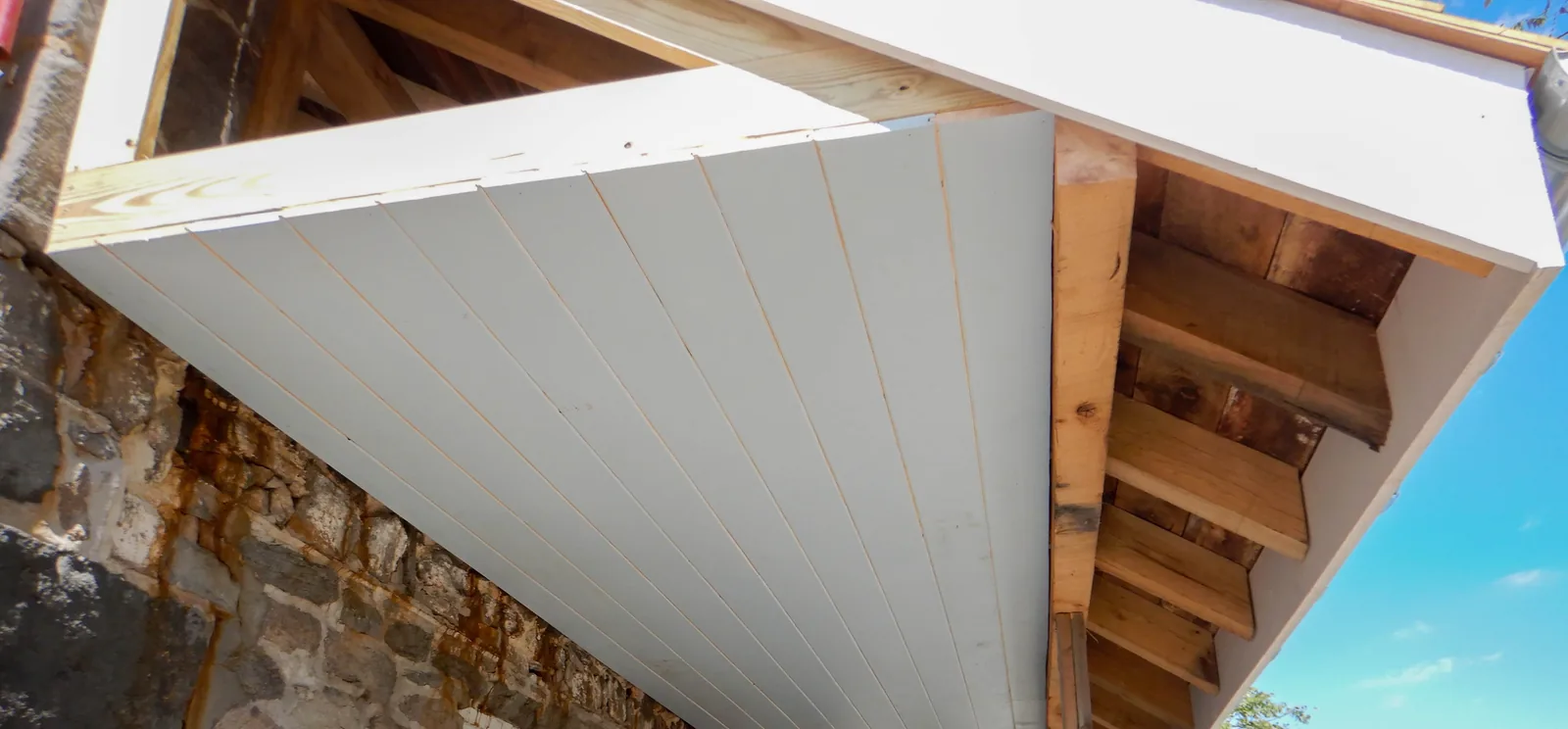New white beadboard porch ceiling planks and exposed rafters seen from below