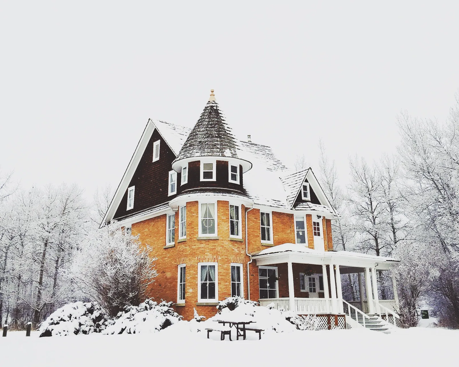 White covered wraparound porch on a brick house under heavy snow