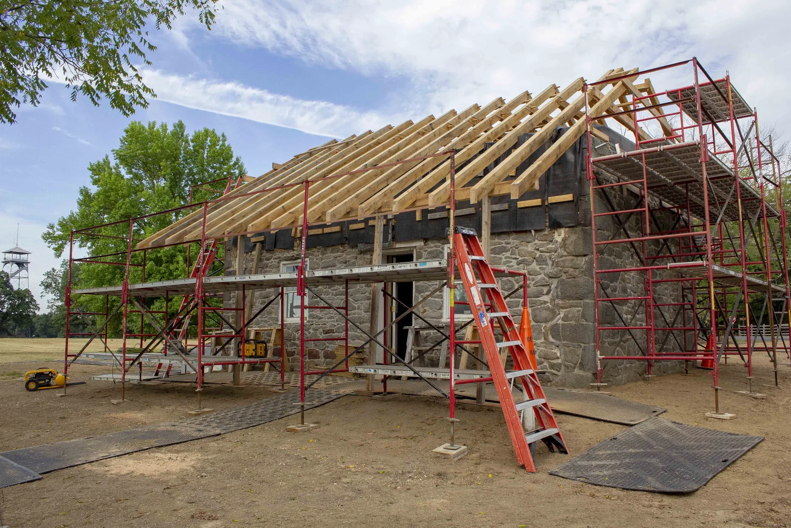 Bare rafters and porch roof framing over a stone house with scaffolding